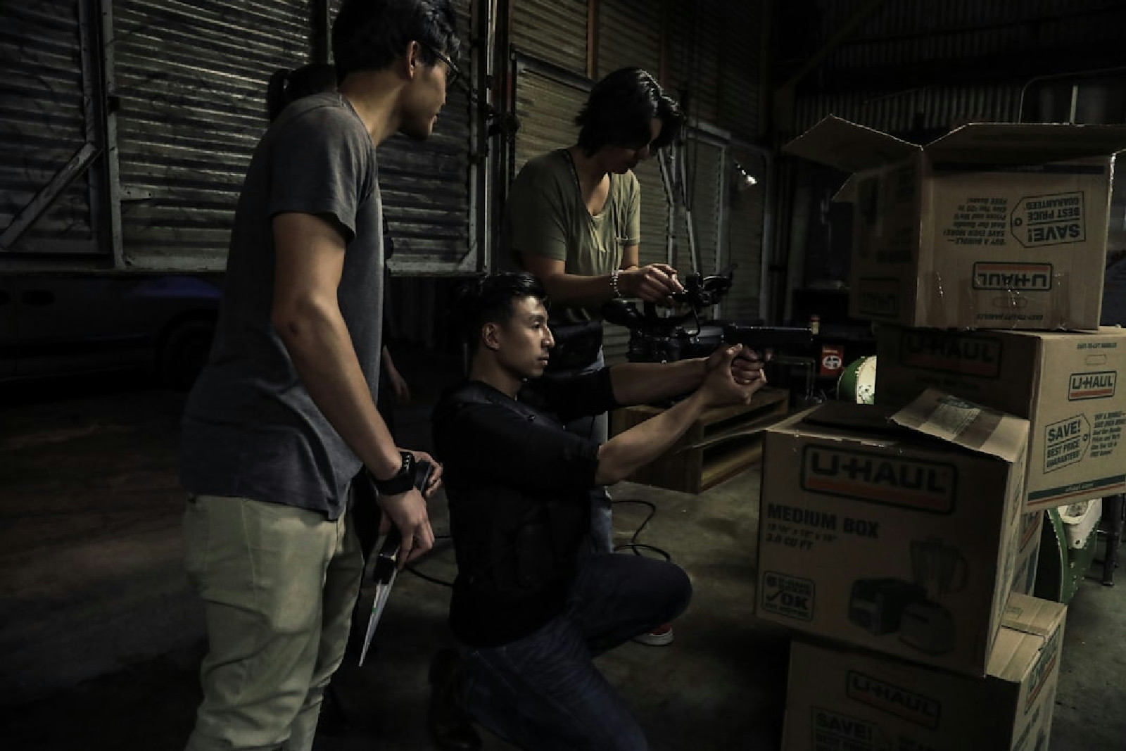 Dois homens diante de um personagem sentado em cenário industrial